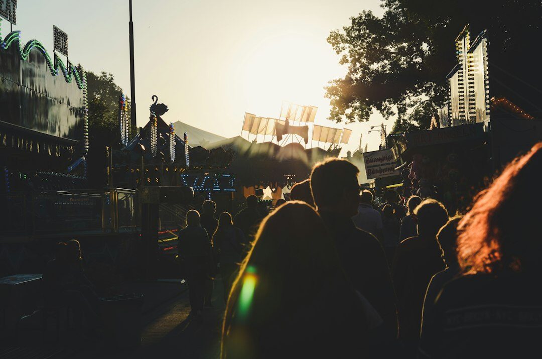 Silhouettes of a crowd watching a brightly lit stage at dusk during a public event